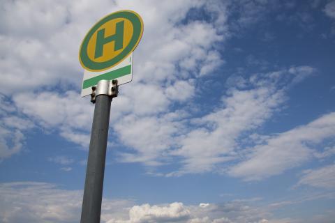 Ein Bushaltestellenschild vor blauem Himmel mit Wölkchen