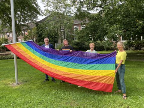 Vier Personen hissen Regenbogen-Flagge an Fahnenmast