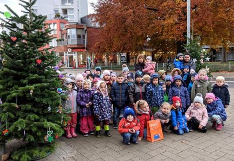 Kindergruppe mit Erziehern vor Weihnachtsbaum draußen