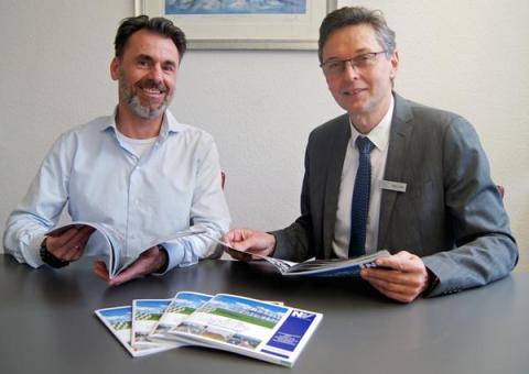 Zwei Männer sitzen am Tisch mit Broschüren in der Hand