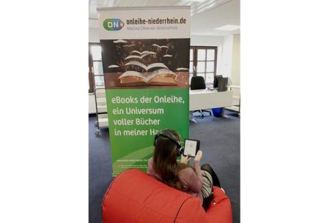 Mädchen auf Sitzsack liest ebook, im Hintergrund Banner der Onleihe