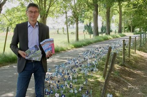 Bürgermeister mit Flyern vor textilen Flachsblüten am Wegrand
