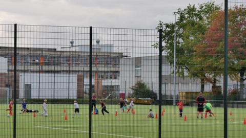 Kinder auf Sportplatz hinter Zaun