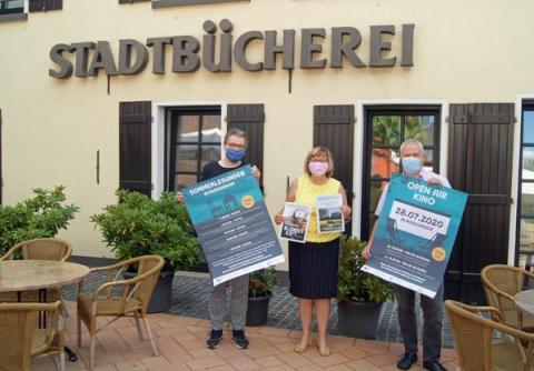 3 Personen mit Plakaten in der Hand vor der Stadtbücherei
