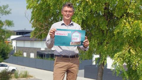 Bürgermeister hält Plakat Heimatpreis hoch