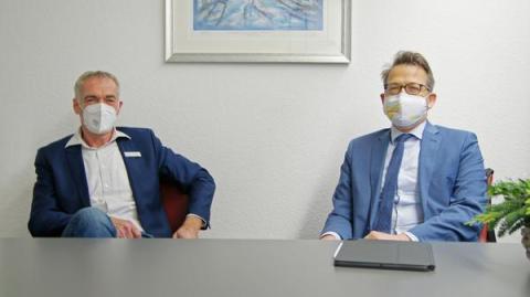 2 Männer mit Masken sitzen am Tisch