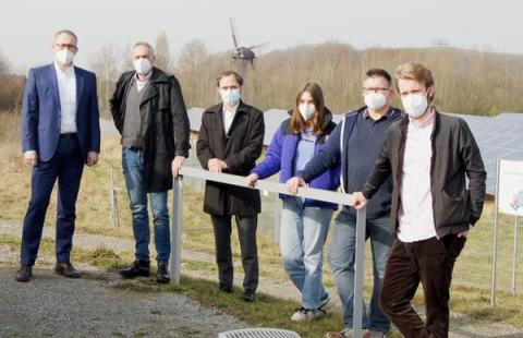 Mehrere Menschen nebeneinander, im Hintergrund ein Solarpark