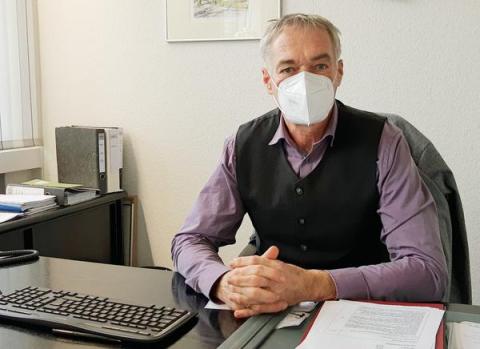 Mann mit Maske am Schreibtisch sitzend