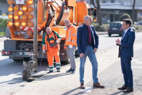 Straßenreinigungsfahrzeug mit zwei Arbeitern, davor zwei Männer die sich unterhalten