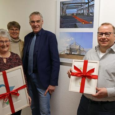 4 Menschen, zwei mit Bilderrahmen in der Hand, vor Fotoausstellung