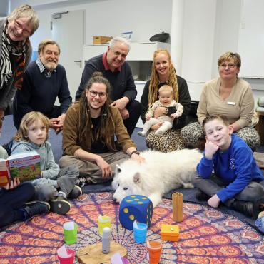 Kinder und Erwachsene im Kreis, ein weißer Hund in der Mitte