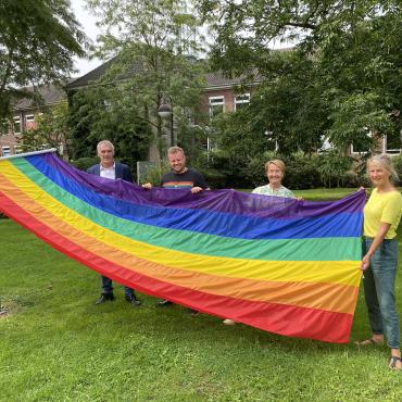 Vier Personen hissen Regenbogen-Flagge an Fahnenmast