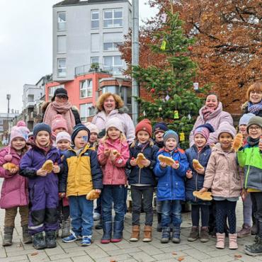 Eine Gruppe Kinder und Erzieherinnen stehen vor Weihnachtsbaum im Freien Eine Gruppe Kinder und Erzieherinnen stehen vor Weihnachtsbaum im Freien
