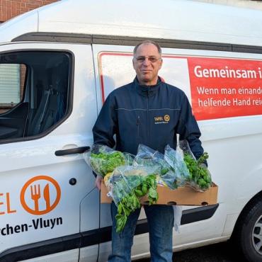 Mann steht mit Gemüsekorb vor Auto